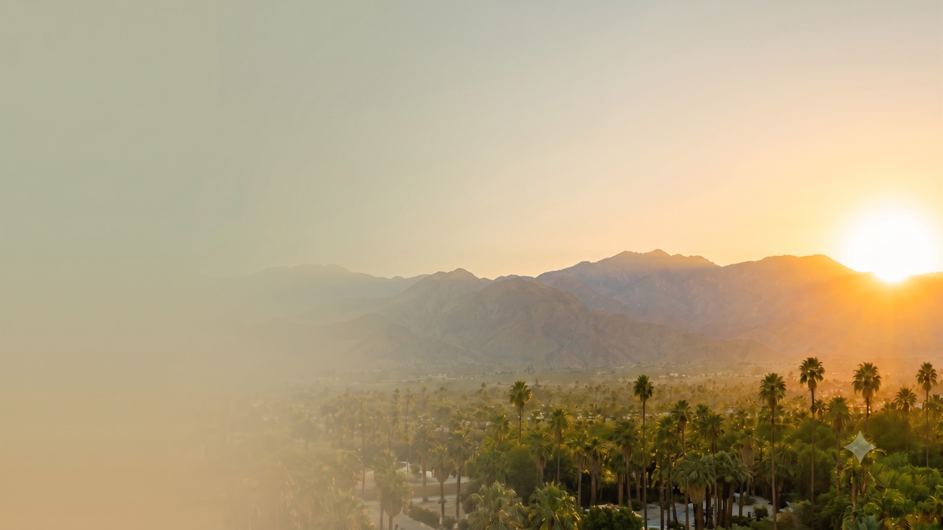 Sunrise over the Coachella Valley, mountains rising above a palm-lined city